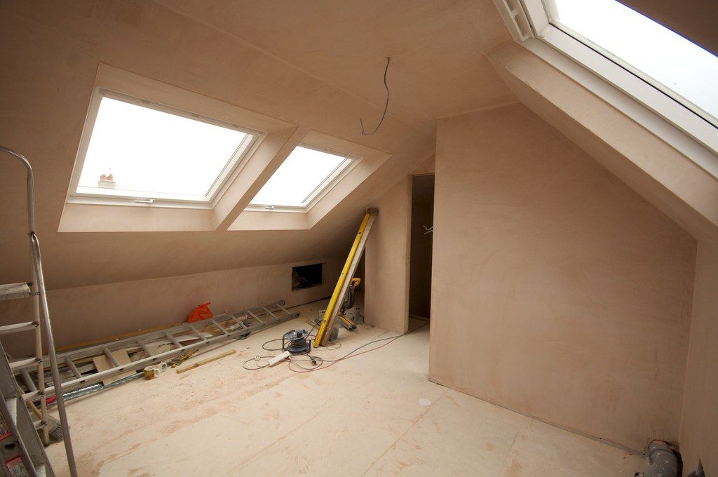 An attic room mid-renovation with freshly plastered walls, skylights and tools on the floor