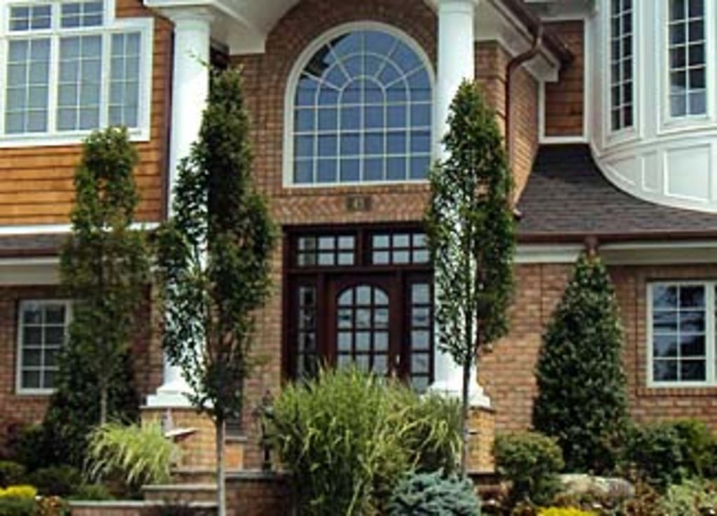 A brick and shingle family home with an arched window, white columns and neatly planted shrubs